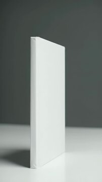 A pristine, vertical white hardback book mockup with a smooth matte cover and sharp edges, centered in a medium video with soft light gray studio background, subtle softbox lighting, and slow