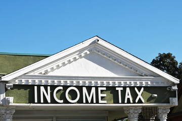Closeup of the words Income Tax  on a building Sign with a blue sky.