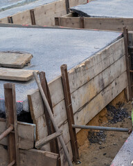 Construction site showing concrete foundation work with wooden forms and excavation visible in a residential area during daylight hours