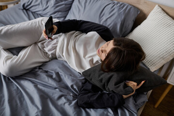 Young woman enjoying a relaxed day in bed while scrolling through her phone