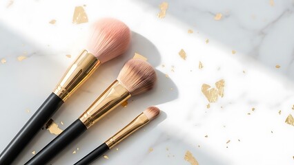 Three professional makeup brushes arranged on a white marble surface with gold accents