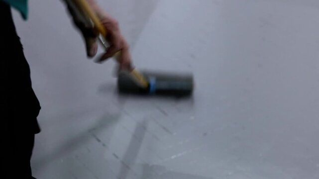 Gray paint application to a herringbone parquet floor by a person with a paint roller, showcasing home renovation and interior design, transforming a parquet floor with gray paint.