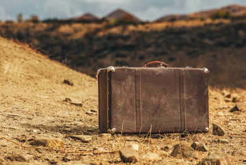 A brown suitcase is sitting on a rocky, dry ground