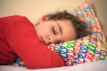 A young girl is sleeping on a bed with a colorful pillow