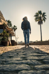 female backpacker walking along a sunlit cobbled street by the sea