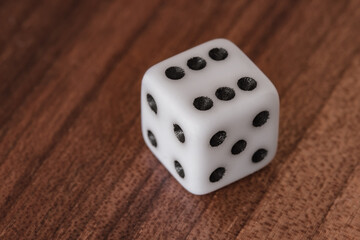 A single white gaming dice rests on dark wood. Dramatically illustrating probability, chance, luck, gambling and the inherent risk of success or danger. Ideal for finance marketing.