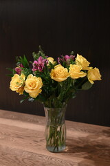 A vibrant floral bouquet featuring soft yellow roses and bright magenta flowers arranged in a clear glass vase against a dark background. Elegant, fresh, themes of celebration, décor, romance.