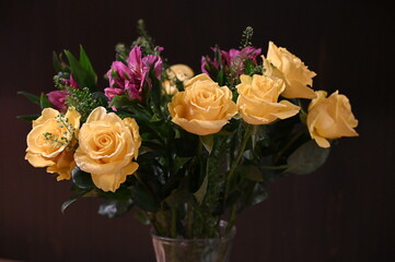 A vibrant floral bouquet featuring soft yellow roses and bright magenta flowers arranged in a clear glass vase against a dark background. Elegant, fresh, themes of celebration, décor, romance.