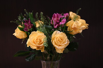 A vibrant floral bouquet featuring soft yellow roses and bright magenta flowers arranged in a clear glass vase against a dark background. Elegant, fresh, themes of celebration, décor, romance.