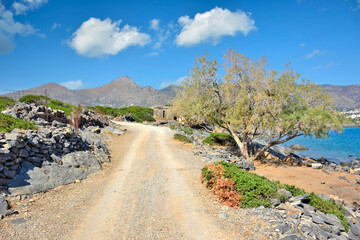 A dirt road  in Kalydon (Spinalonga) peninsula near the Elounda town in Crete, Greece. Beautiful blue sky with white clouds in the background.
