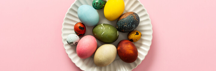 A collection of vibrant Easter eggs in various colors is artfully arranged on a white plate, set against a soft pink background, capturing the essence of the holiday's decorations, banner