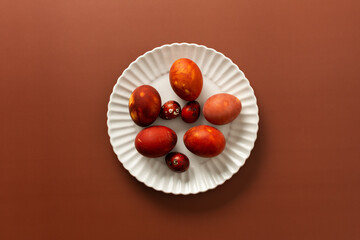Vibrant Easter eggs in various shades of red and orange are beautifully arranged on a white plate, adding charm to the festive atmosphere of the season