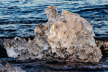 Glowing crystalline iceberg washing ashore on Diamond Beach with splashing waves