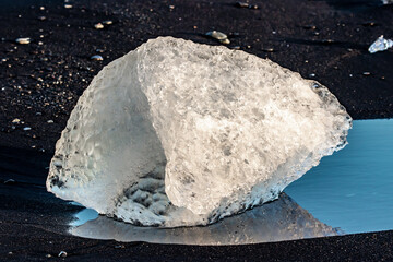 Large transparent iceberg block resting on black volcanic sand at Diamond Beach