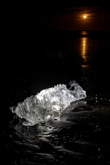 Moonlight reflecting on the ocean behind a glacial ice chunk at Diamond Beach