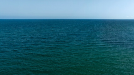 Fototapeta premium Aerial view of the deep blue sea surface. In the background, on the horizon, a clear, cloudless sky. Seascape concept.