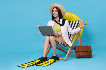 Businesswoman with laptop and flippers in deck chair on light blue background © New Africa