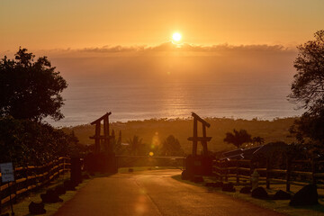 Tropical sunset over ocean with scenic road, wooden gate and warm golden light in Hawaii