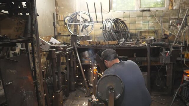 Worker in protective mask welding metal construction at industrial production. Welder doing joint between two steel details. Man welding parts of the metal detail together. Manual labor with metal