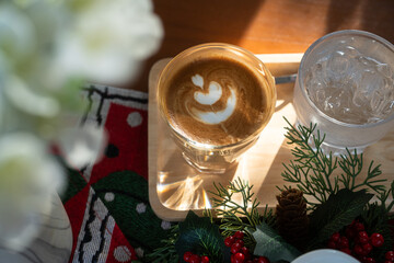 Close up of Hot coffee latte with latte art milk foam in cup mug with Xmas decors and Xmas tree baubles on wood desk Celebrating Merry Christmas and New year,Merry x-mas