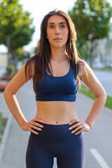 young woman runner in athletic wear stands confidently on city street