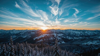 Snow-covered mountains at sunrise with the sun rising behind the peaks, clear sky with clouds, and a forest in the foreground.
