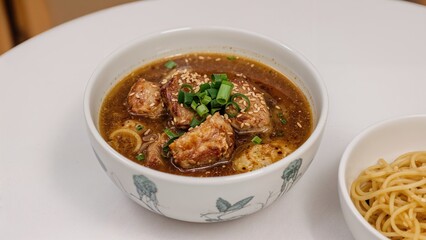 Fototapeta premium Bowl of hot soup with meatballs, broth, and chopped green onions, accompanied by a side of spaghetti. Traditional Asian and Italian cuisine. Food and dining.