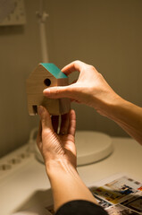 Hands assembling a small wooden house model with a green roof