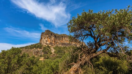 Fototapeta premium Rock formation and tree in a natural landscape with blue sky and clouds. Nature and scenery, outdoor environment. The concept of landscape and geological features.