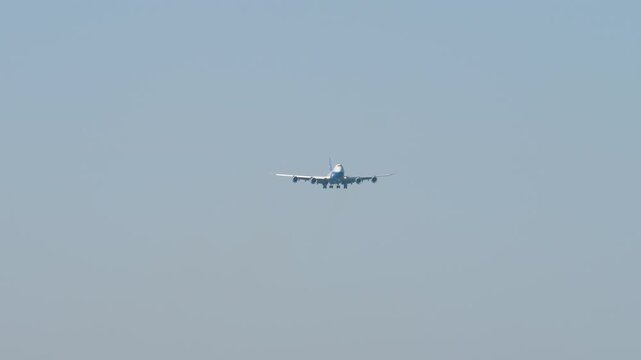 Large aircraft with an unrecognizable livery approaching landing, front view long shot. Airplane in blue sky background. Travel concept