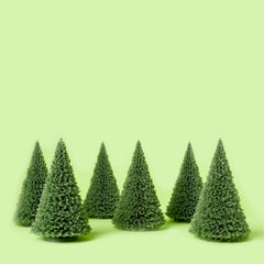 A clean, minimalist composition featuring a row of small artificial Christmas trees arranged against a pastel green background. The soft color palette and simple layout create a modern, festive look.