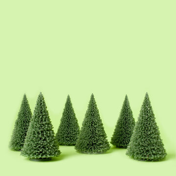 A clean, minimalist composition featuring a row of small artificial Christmas trees arranged against a pastel green background. The soft color palette and simple layout create a modern, festive look.