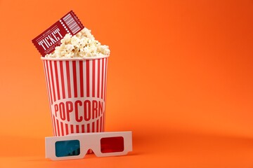 Tasty popcorn in paper cup, 3D glasses and movie ticket on orange background. Space for text