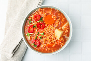 Delicious lentil soup with vegetables in bowl on white tiled table, top view