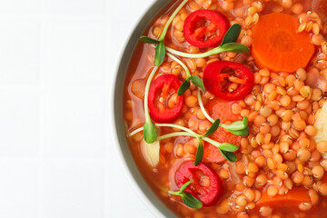 Delicious lentil soup with vegetables in bowl on white table, top view. Space for text