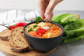 Woman salting delicious lentil soup at grey table, closeup
