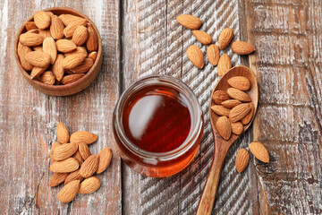 Honey in jar and almonds on wooden table, above view