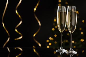 Merry Christmas and Happy New Year. Flute glasses with sparkling wine and serpentine streamers on black background against blurred lights. Space for text