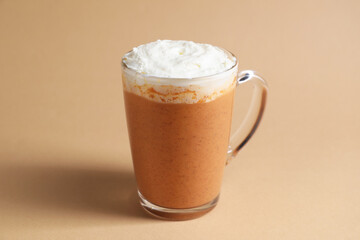 Delicious pumpkin latte with whipped cream in glass cup on beige background, closeup