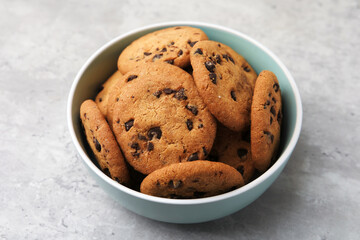 Delicious chocolate chip cookies in bowl on gray textured table, closeup
