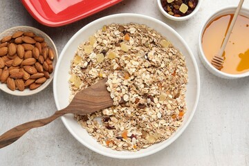Making granola. Bowl of oat flakes, honey and dried fruits on light grey table, flat lay