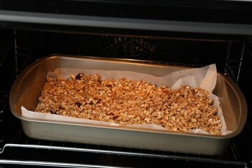 Tasty granola with dried fruits baking in oven, closeup