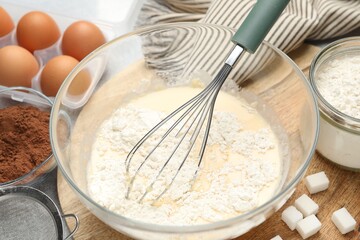 Different ingredients for dough and whisk on table, closeup