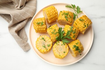 Pieces of boiled corncobs with parsley on white marble table, top view