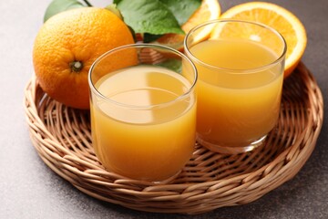 Fresh orange juice, fruits and green leaves on grey table, closeup