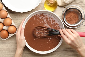 Woman mixing liquid chocolate dough with whisk at wooden table, top view