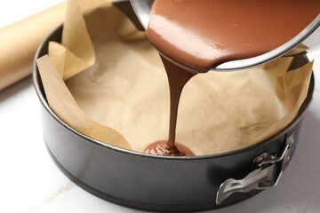 Pouring liquid chocolate dough into baking dish at white marble table, closeup