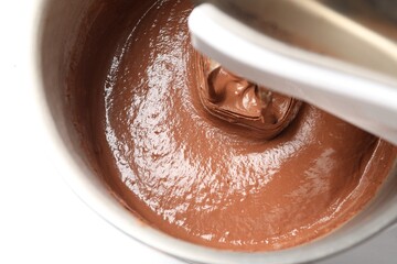 Mixing chocolate dough in bowl at white table, top view