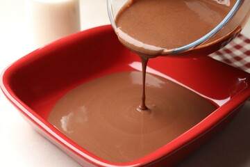 Pouring liquid chocolate dough into baking dish at white table, closeup