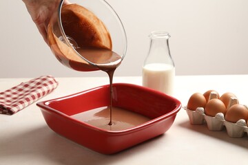 Woman pouring liquid chocolate dough into baking dish at white table, closeup